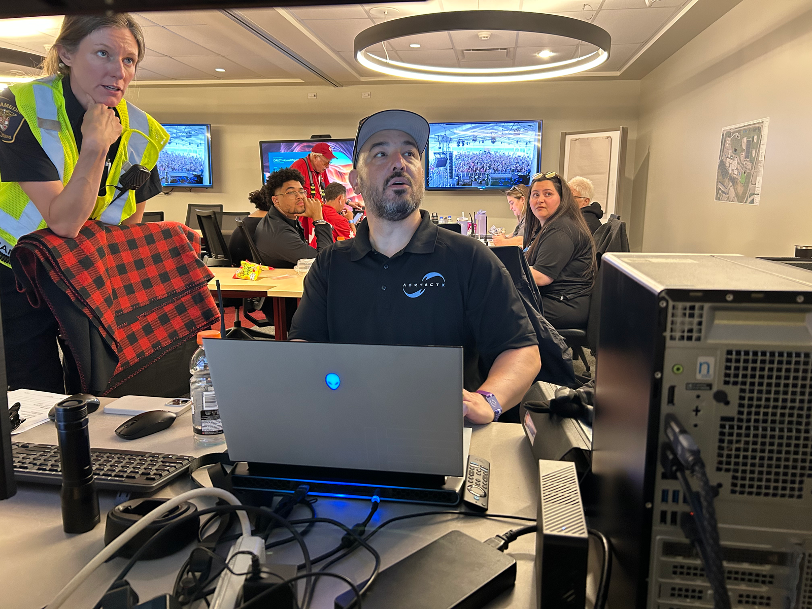 AertactX team member at a laptop alongside event personnel, with live event footage on screens behind them